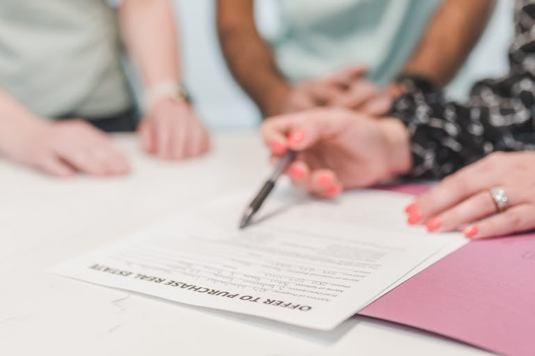 Close-up of people reviewing and signing an offer to purchase real estate document.