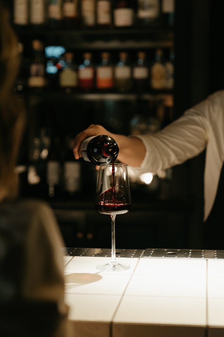 An elegant scene of red wine being poured at a dimly lit bar counter.