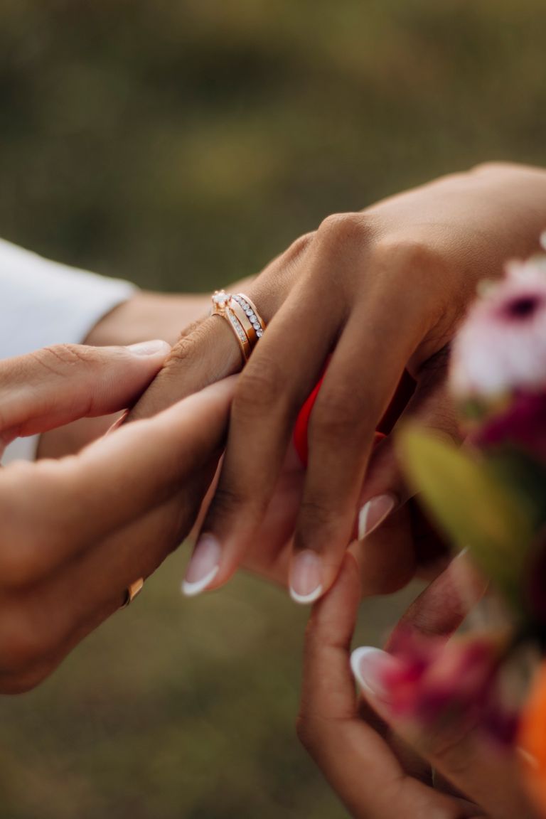 Intimate moment of couple exchanging rings during a wedding ceremony with floral background.