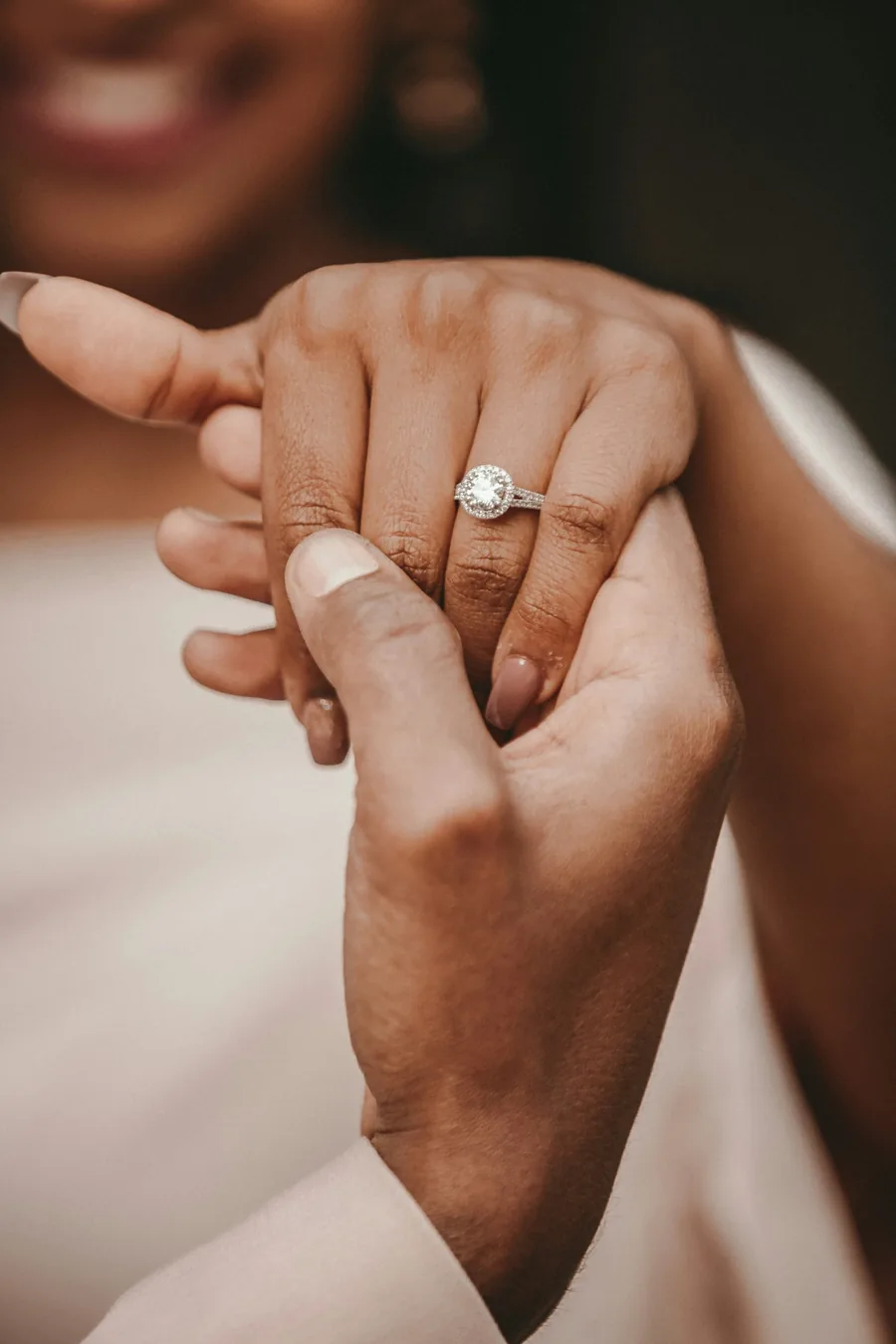 Close-up of a couple holding hands, showing a diamond engagement ring on one partner's finger.